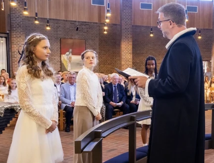 Tre konfirmander står ved knæfaldet foran præsten, der læser et konfirmationsord op for den ene konfirmand. 