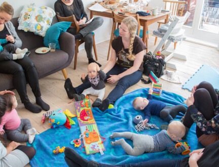 En mødregruppe er i en stue med små børn på tæppe