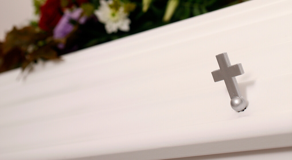 Et lille kors på en hvid kiste, som er pyntet med blomster.