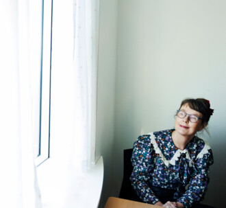 Præst i blomstret bluse sidder ved bord og kigger ud af vindue