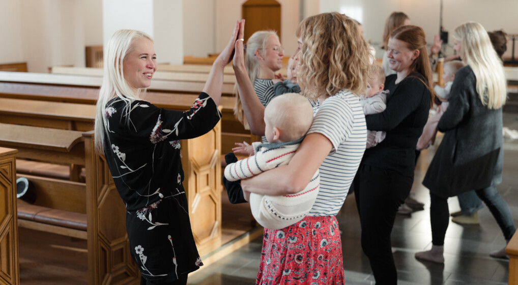 To kvinder giver hinanden et high five til babysalmesang i en kirke