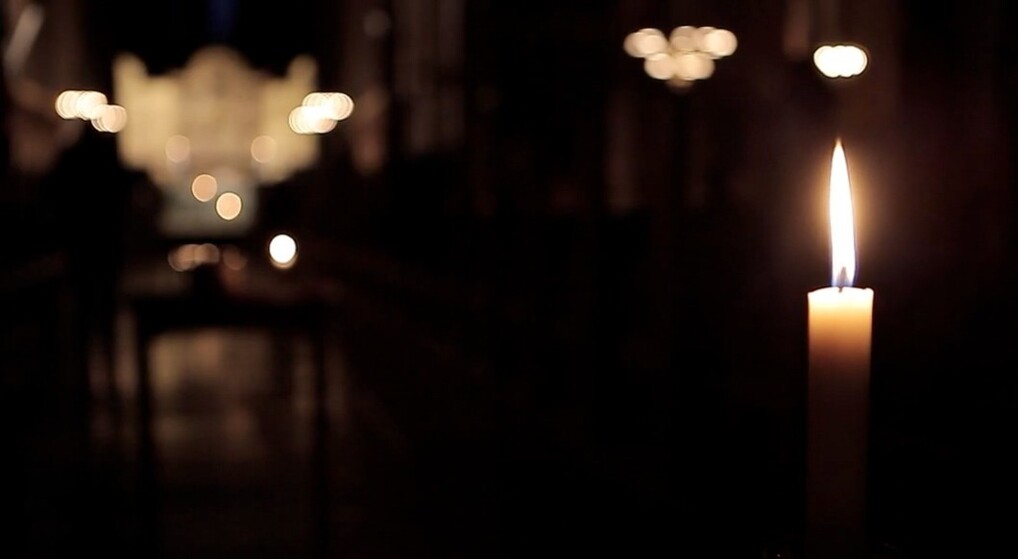 Billede af tændt stearinlys i en mørk kirke