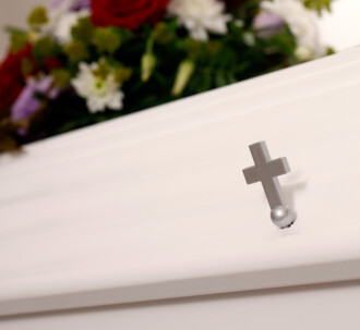 Et lille sølvfarvet kors på en hvid kiste.