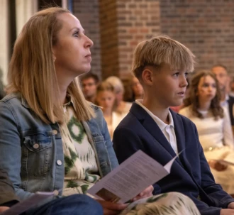 En konfirmand og hans mor sidder i kirken og lytter opmærksomt under en konfirmation.