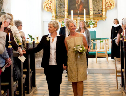 Et brudepar går ned ad kirkegulvet sammen efter vielsen, mens præsten står oppe ved alteret