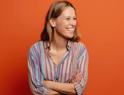  Lea Korsgaard, chefredaktør på Zetland og forfatter til bogen, Inden året er omme, står foran orange baggrund med korslagte arme