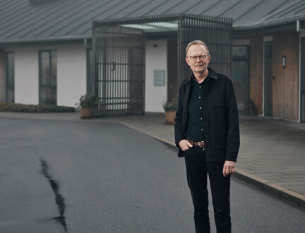 Tidligere hospicepræst Ole Raakjær foran sognegård med den ene hånd i lommen