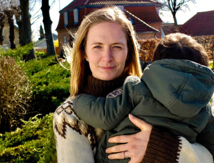 Ung kvinde i striktrøje holder sit barn i armene i villakvarter