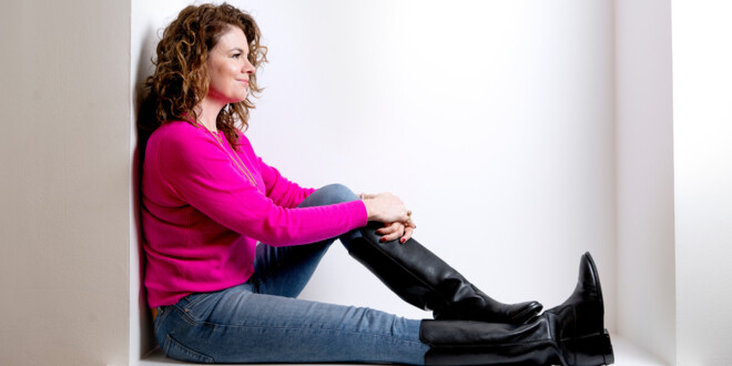 Julia Lahme sidder med siden til op ad en mur iført pink bluse, jeans og lange støvler