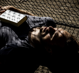 Musiker Kjartan Arngrim ligger på en tennisbane med en højskolesangbog på brystet