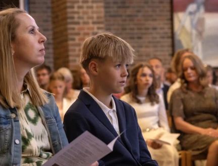 En konfirmand og hans mor sidder i kirken og lytter opmærksomt under en konfirmation.